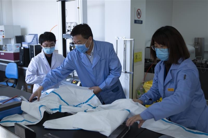 圖為趙玉杰（中）檢查醫(yī)用防護(hù)服應(yīng)急檢測(cè)工作。