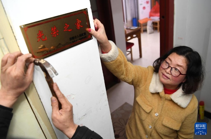 合肥市包河區(qū)常青街道工作人員在居民魏松梅（右）家門口懸掛“光榮之家”牌（2019年1月14日攝）。新華社記者 劉軍喜 攝
